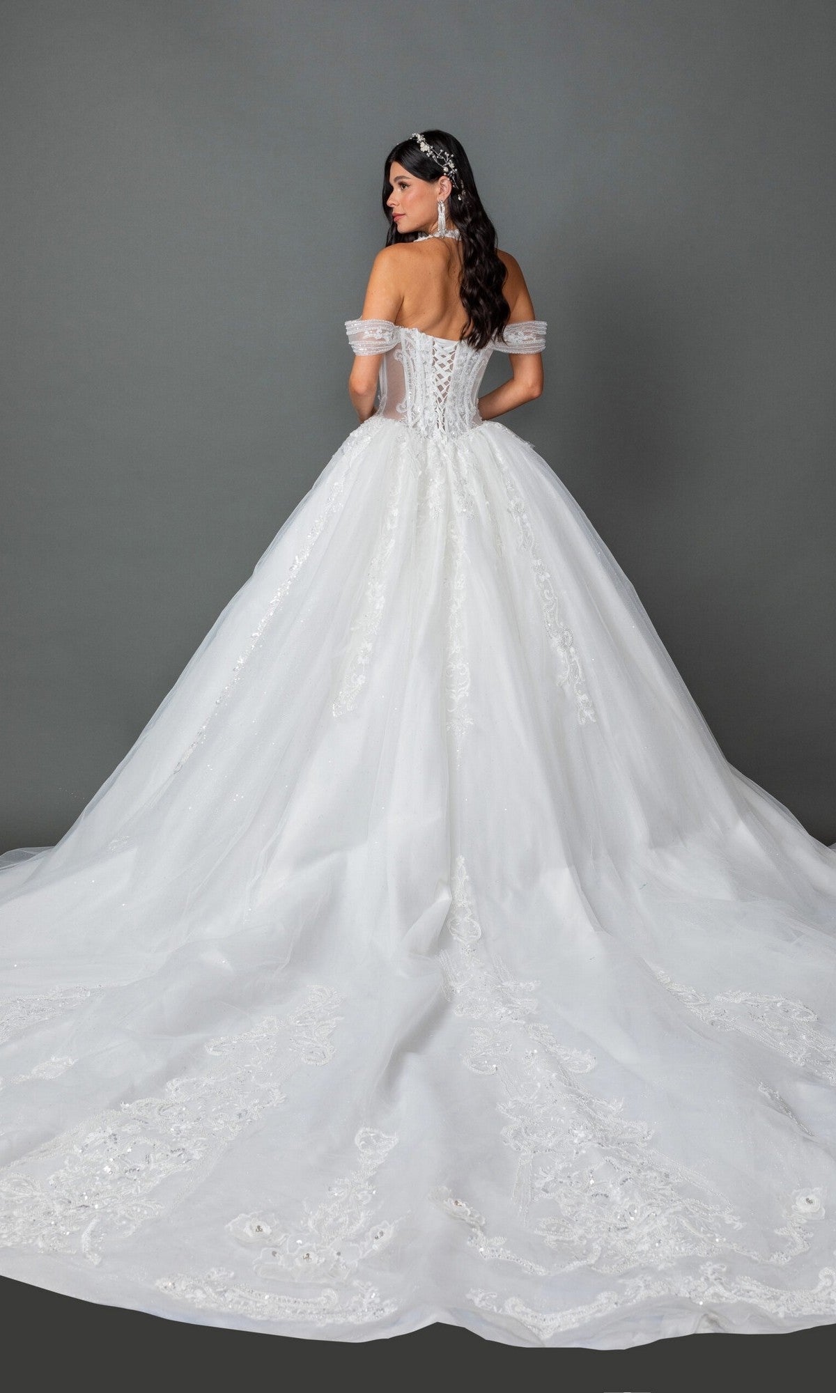 A woman wearing the Long Wedding Dress: Dancing Queen 0324โan off-the-shoulder white lace ballgown featuring delicate lace details and a long trainโstands against a plain gray background.